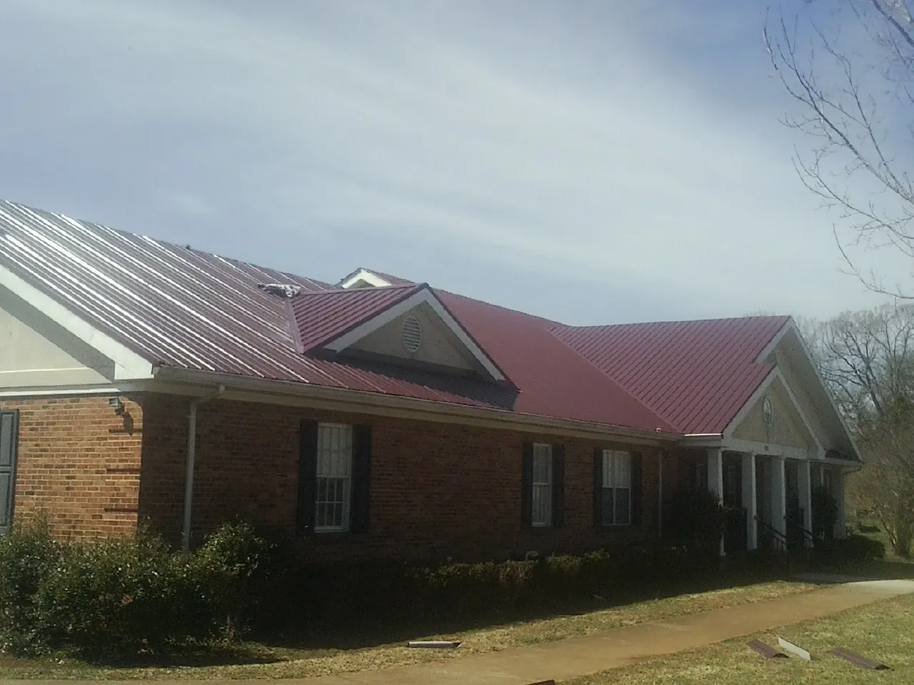 Red metal roof with gabled entries on a long brick building, from a Hail Damage Roof Repair job in Pedricktown