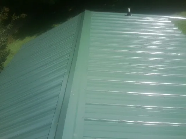 New green metal panels meeting at the ridge of a roof — Flat Roof Repair work by our crew in Pedricktown