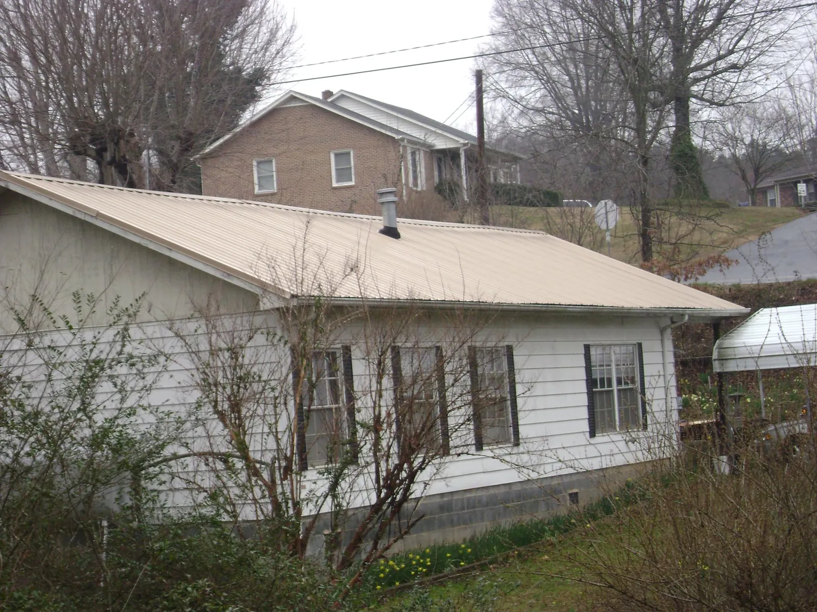 Tan metal roof on a white sided house set into a hillside — Commercial Roofing by Roofing Brothers in Pedricktown